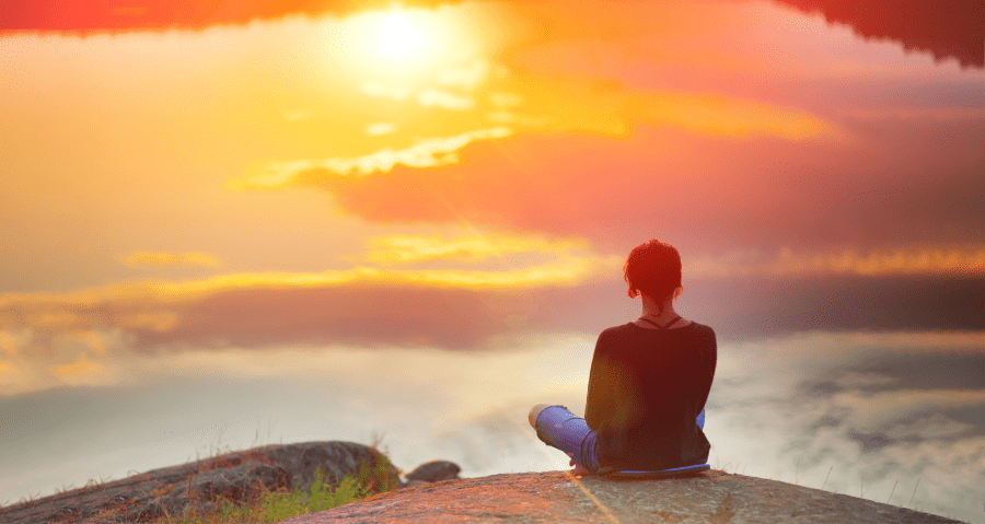 A woman sits on a mountain and looks at the clouds